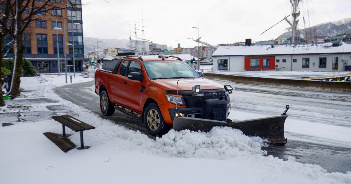 An orange pickup with a snow plow clearing a snowy street