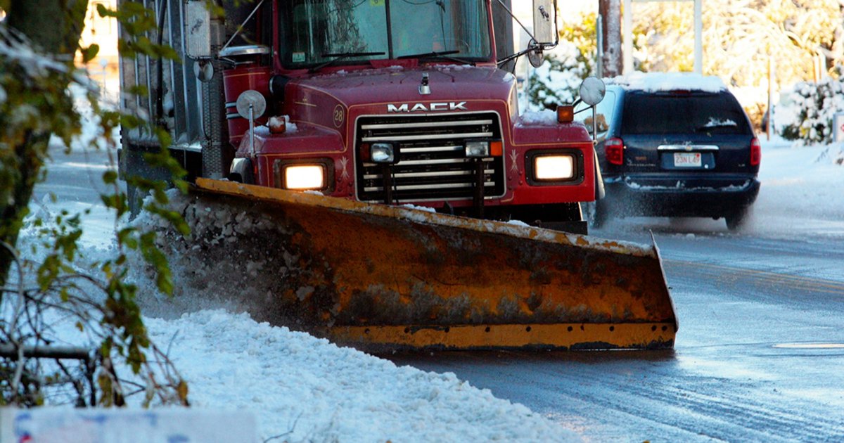 A red plow truck pushing snow off a residential street