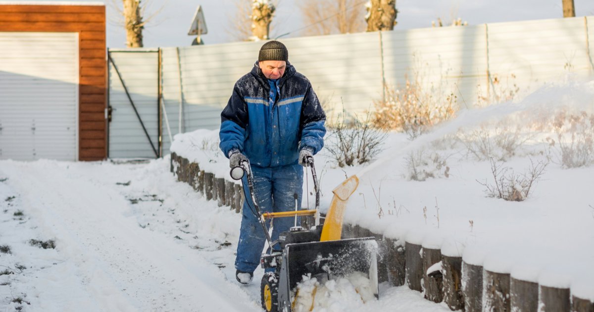 A man clearing a snowy driveway with a snow blower