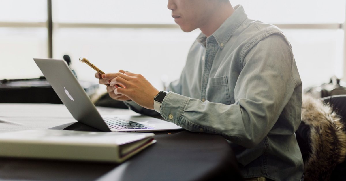 A man working at a laptop with his phone in hand